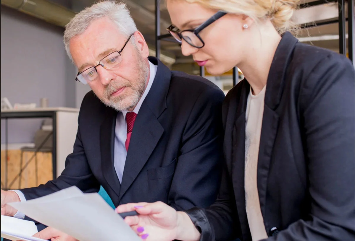 01-Declaraciñon de la renta en RM Consulting – Expertos en recursos humanos Hombre mayor y mujer joven en traje revisan documentos juntos en oficina moderna, representando una sesión de asesoría laboral. Foto de freepik.